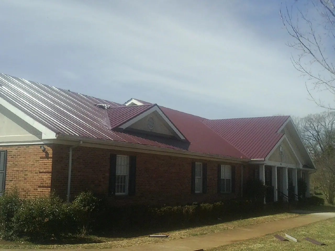 Red metal roof with gabled entries on a long brick building, from a Hail Damage Roof Repair job in Costa Mesa