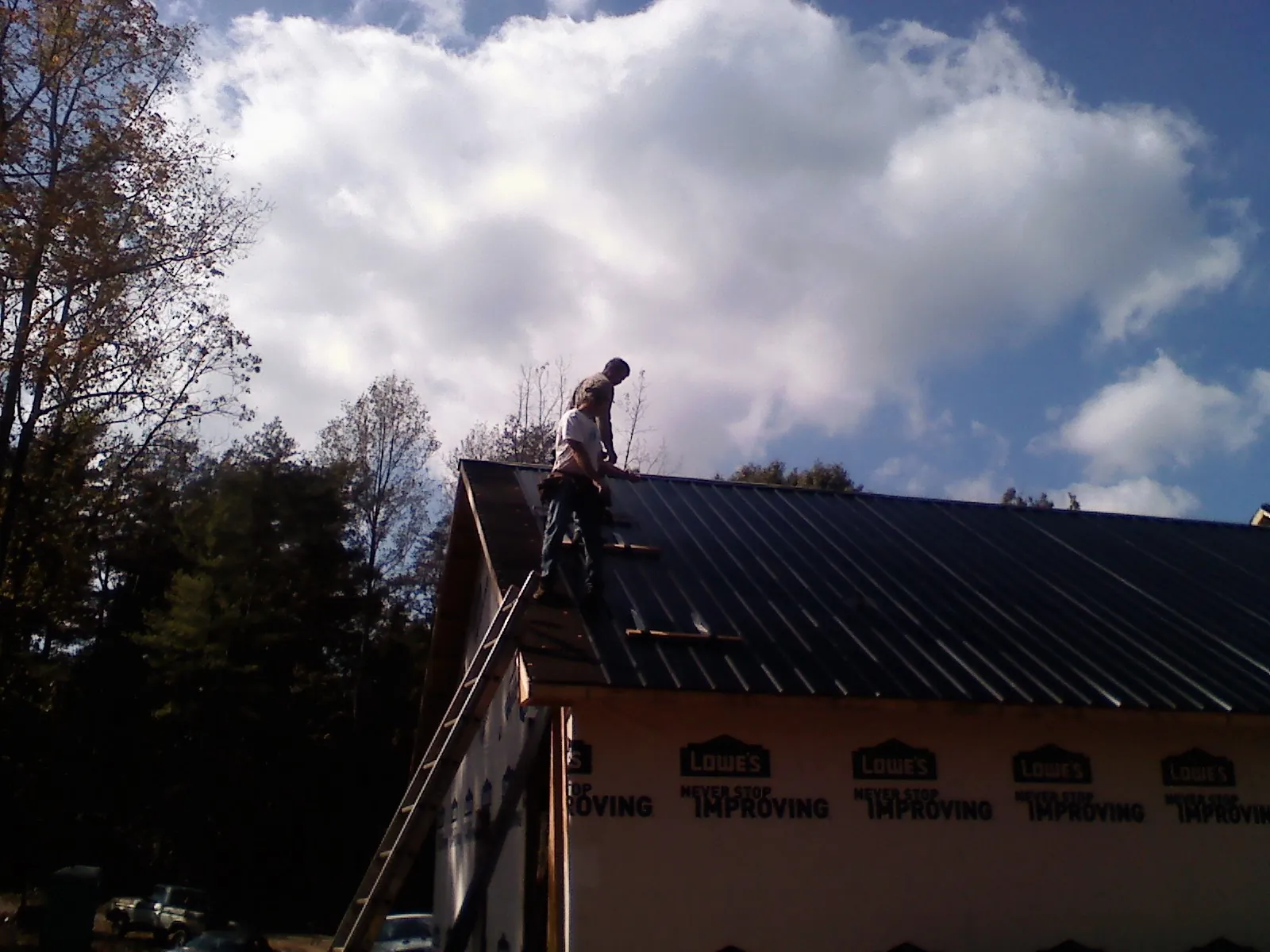 Roofer fastening dark metal panels high against a cloudy sky, from a Roof Inspection job in Costa Mesa